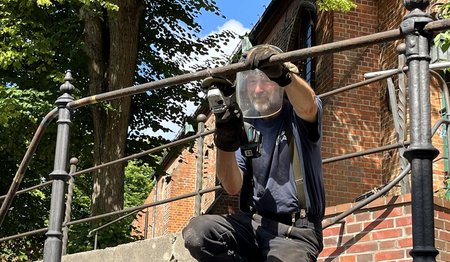 Ein Arbeiter schleift einen Metallhandlauf vor einer Kirche
