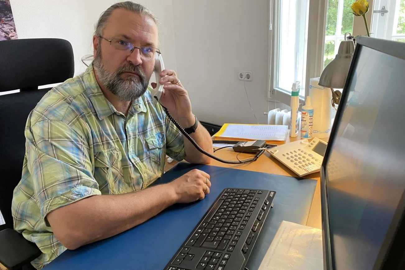 Mann in kariertem Hemd sitzt am Schreibtisch und telefoniert.