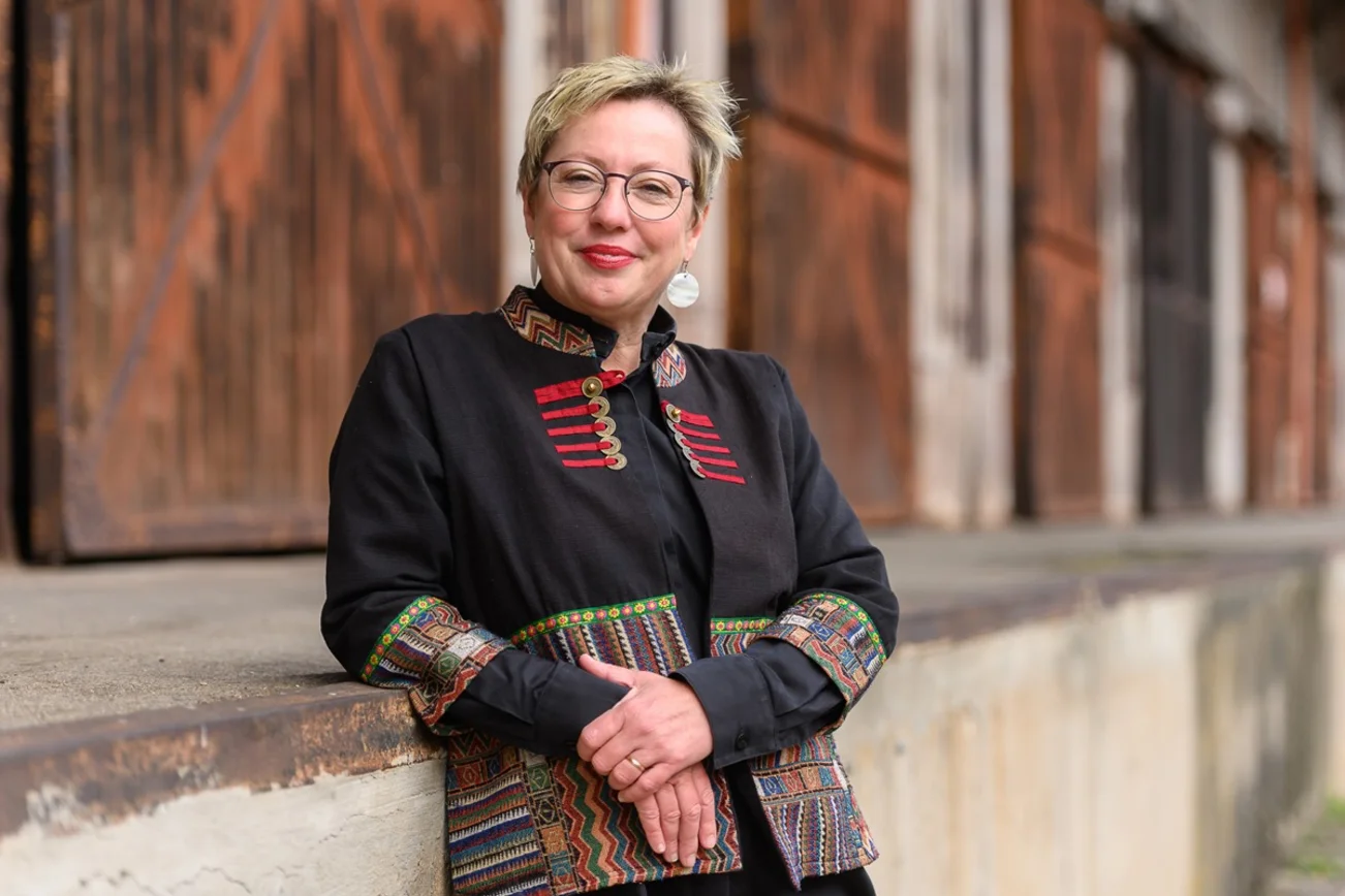 Eine Frau lehnt an einer Brüstung und schaut freundlich in die Kamera.