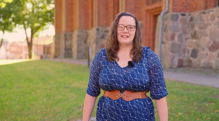 Eine Frau in blauem Kleid steht auf einer Wiese vor einer Kirche.