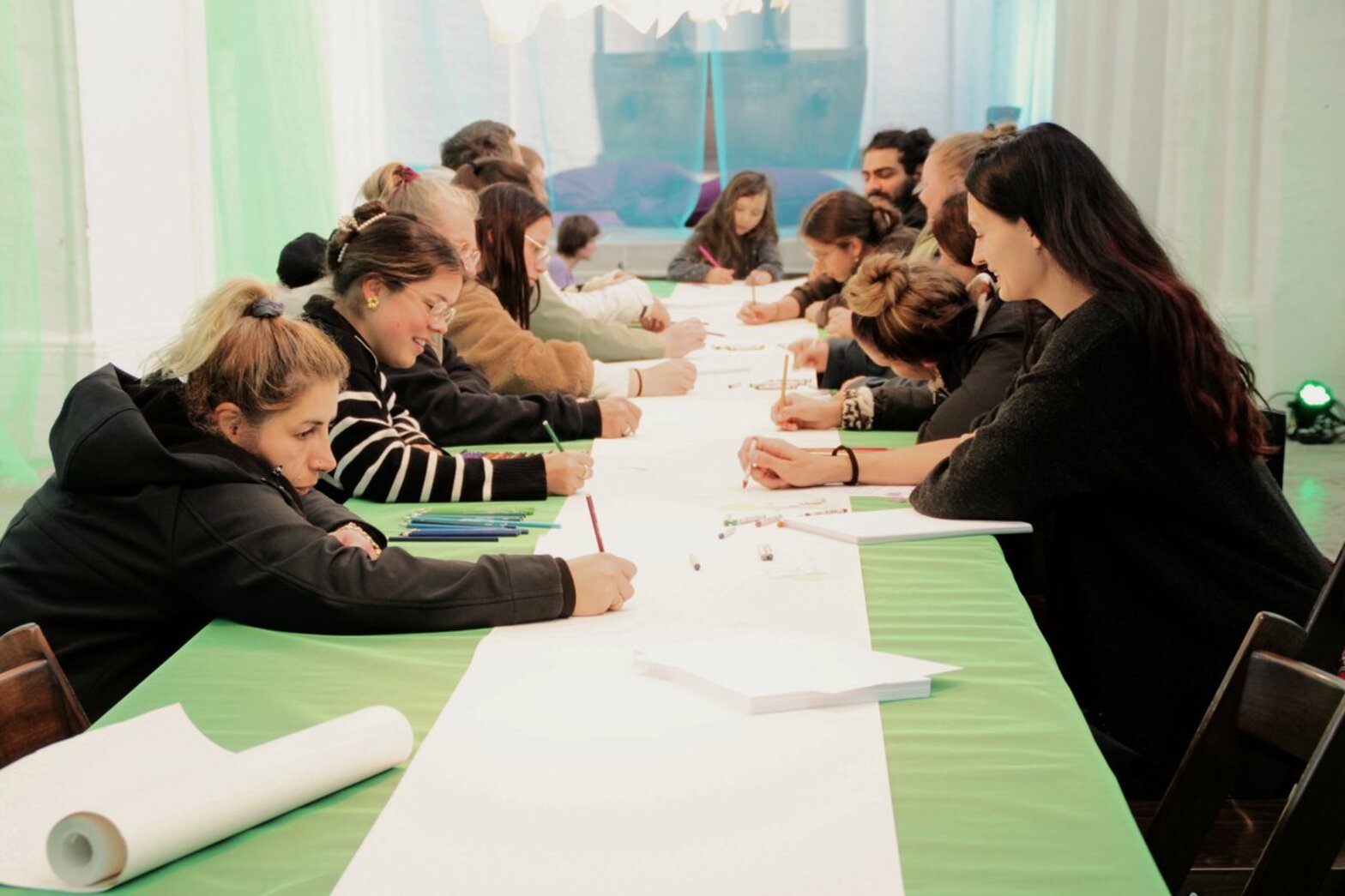 Mehrere junge Menschen sitzen an einem langen Tisch und zeichnen.