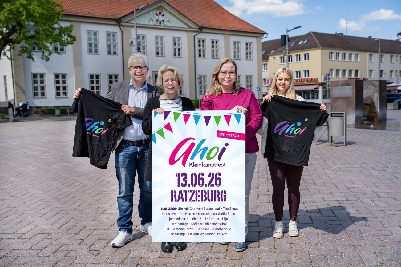 Vier Menschan halten ein Plakat und lächeln in die Kamera.