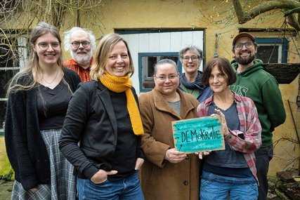 Sieben Frauen und Männer stehen als Gruppe zusammen und zeigen ein Schild mit der Aufschrift Demokratie. - Copyright: Gesa Hollaender