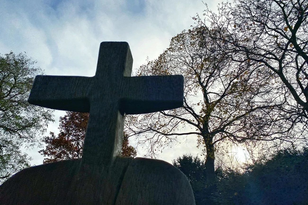 Ein hölzernes Kreuz ragt auf einem Friedhof gen Himmel. 
