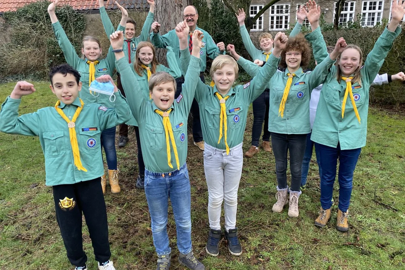 Kinder in Pfadfinder-Kluft strecken voll Freude die Arme in die Höhe. 
