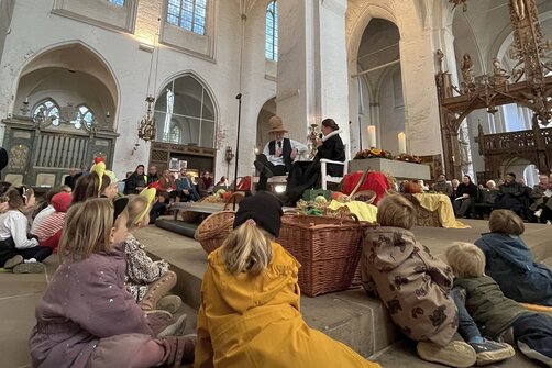 Kinder liegen und sitzen rund um einen Altar vor dem eine Pastorin und Pastor etwas erzählen..