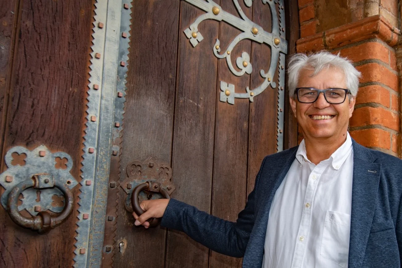 Ein Mann steht lächelnd vor einem Kirchenportal.