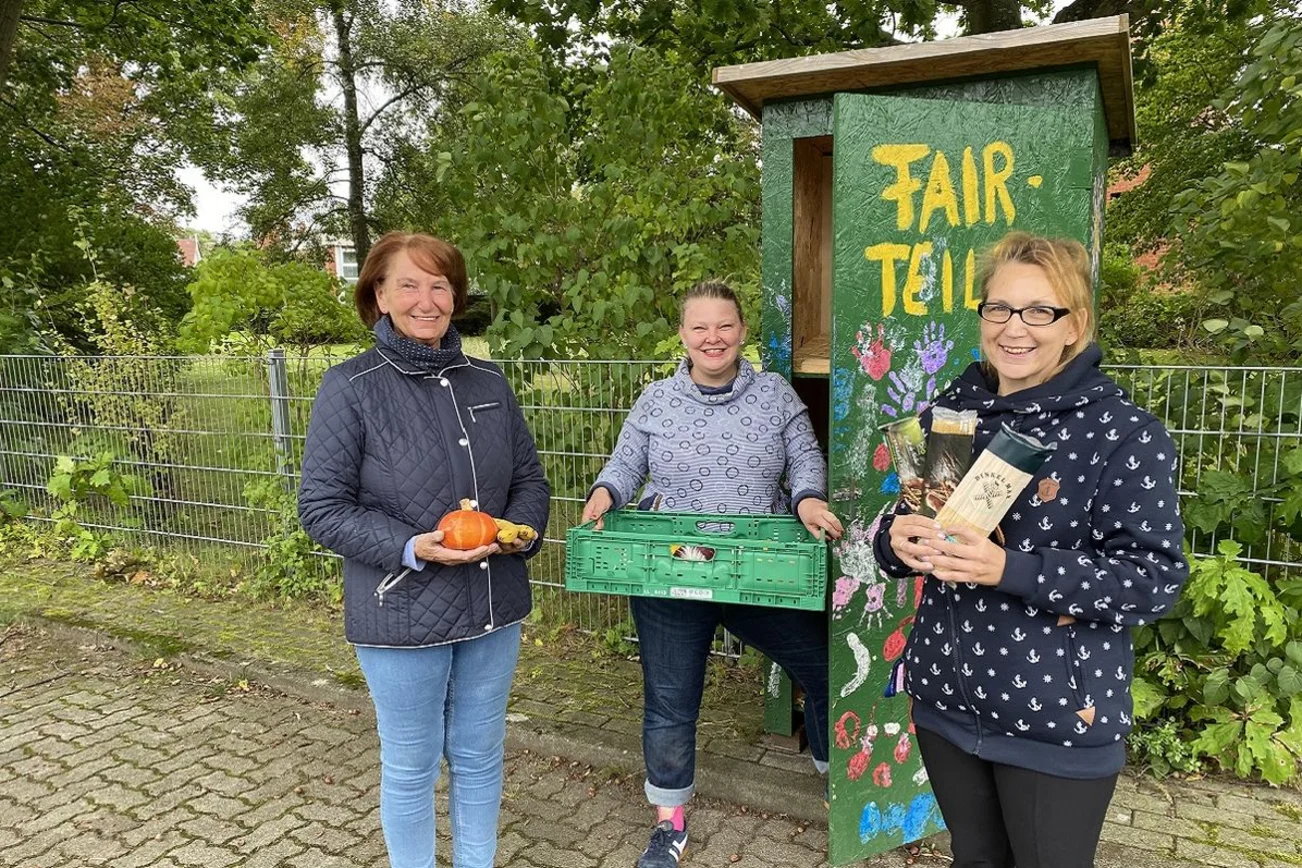 Drei Frauen stehen mit Obst und Konserven vor einem grünen Schrank und lächeln in die Kamera.