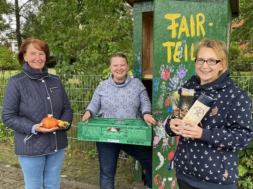 Drei Frauen stehen mit Obst und Konserven vor einem grünen Schrank und lächeln in die Kamera.