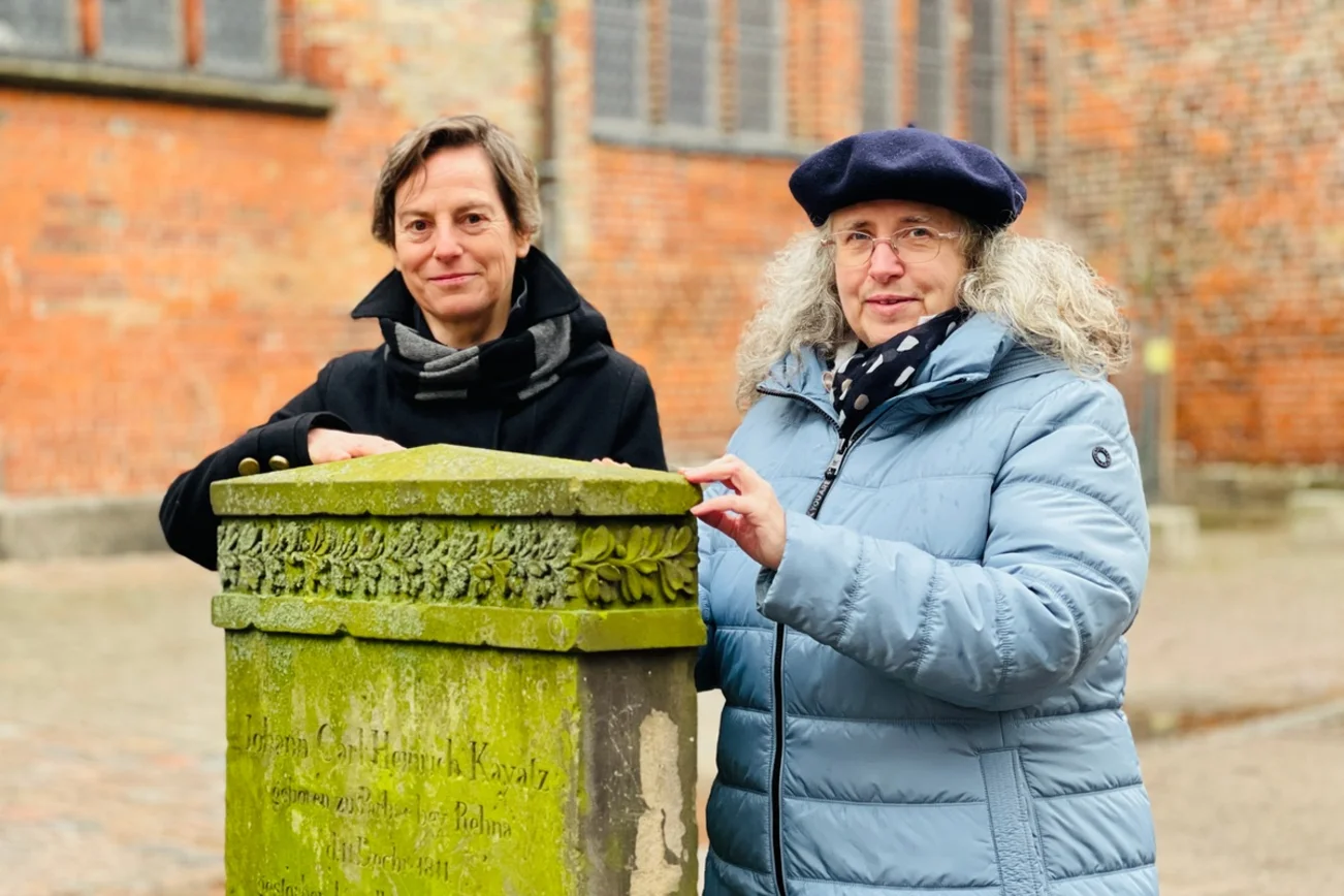 Zwei Frauen lehnen sich an einen alten Grabstein