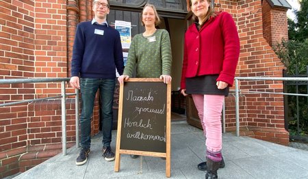 Drei Personen stehen vor dem Eingang einer Kirche. 