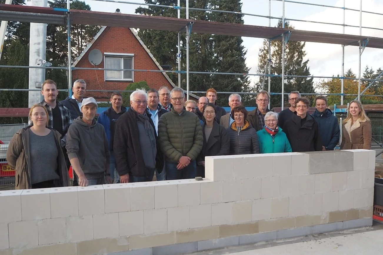 Eine Gruppe Menschen steht an einer hellen Mauer.