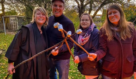 Personen stehen lächelnd im Garten mit Marshmallows.