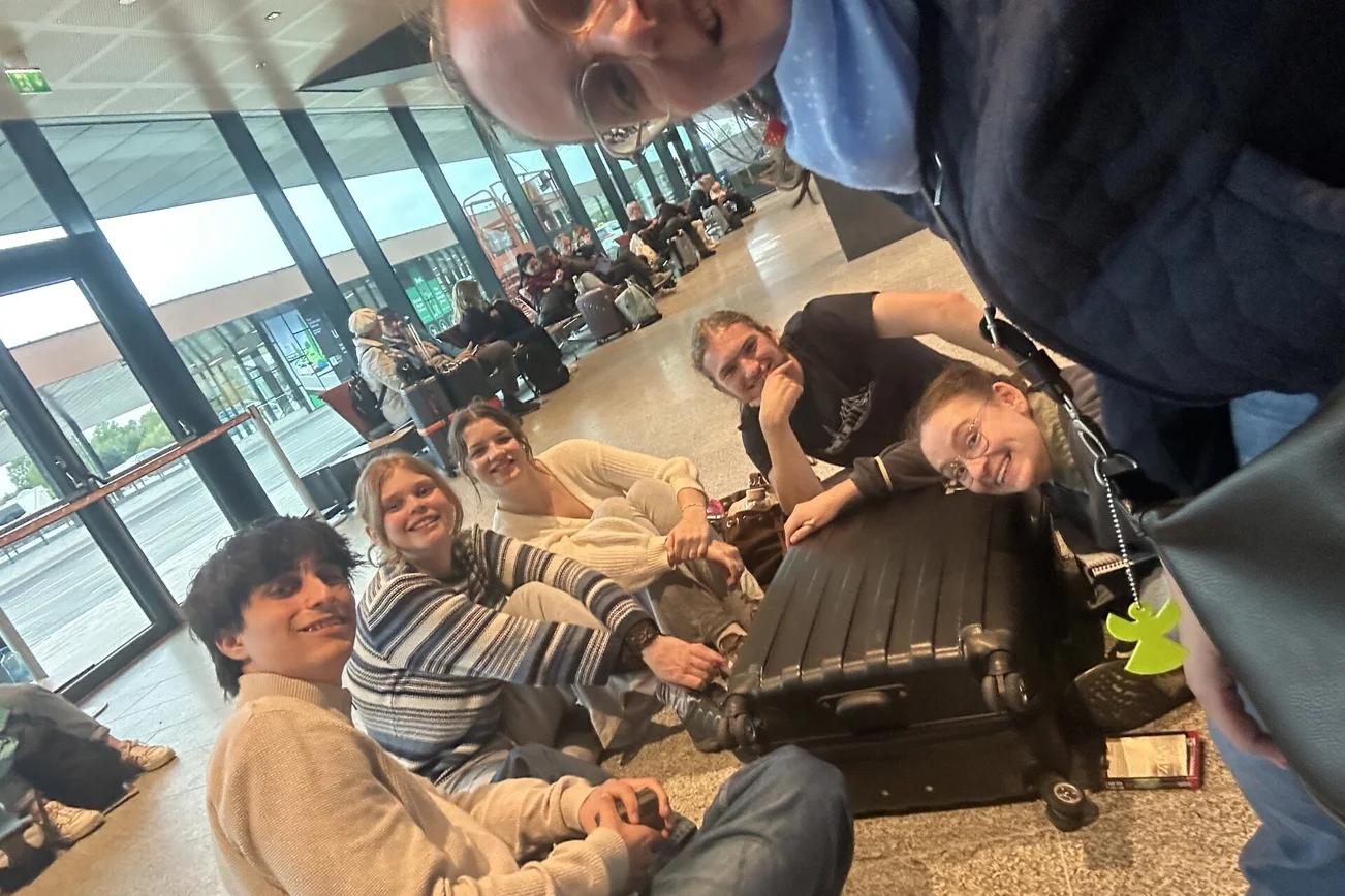 Junge Menschen sitzen mit ihren Koffern auf dem Flughafenboden.