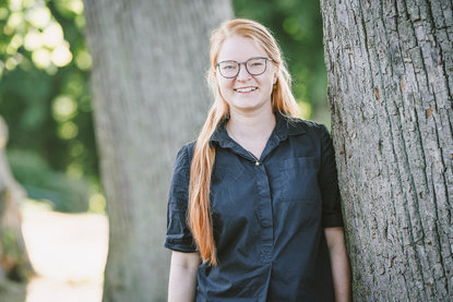 Junge Frau mit Brille lehtn an einem Baum und guckt freundlich in die Kamera. - Copyright: Guido Kollmeier