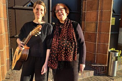 Zwei Frauen stehen vor einem großen Tor und eine Frau trägt eine Gitarre - Copyright: Sabine Loredo Silva