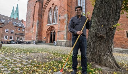 Ein Mann steht mit einem Rechen auf einem Kirchhof.