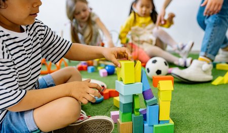 Kinder spielen mit Bauklötzen auf einem grünen teppich