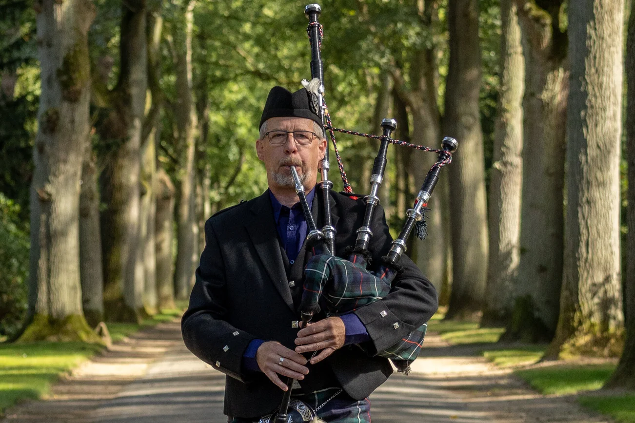 Ein Mann, umgeben von Bäumen, spielt Dudelsack.