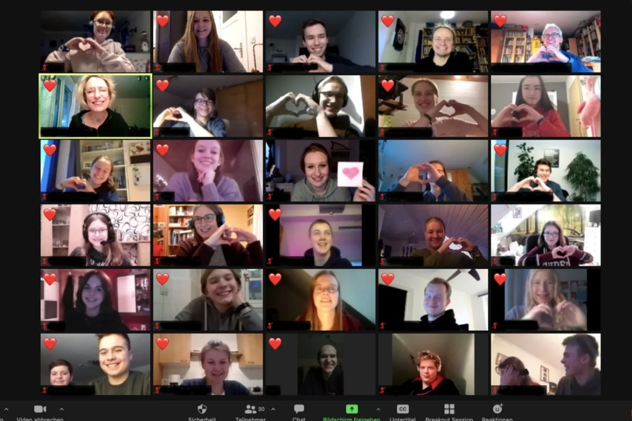 Ein Bildschirmfoto einer Zoom-Konferenz. Auf den Videokacheln sind die Teilnehner:innen zu sehen, einige haben ein Herz obel links im Bild. 