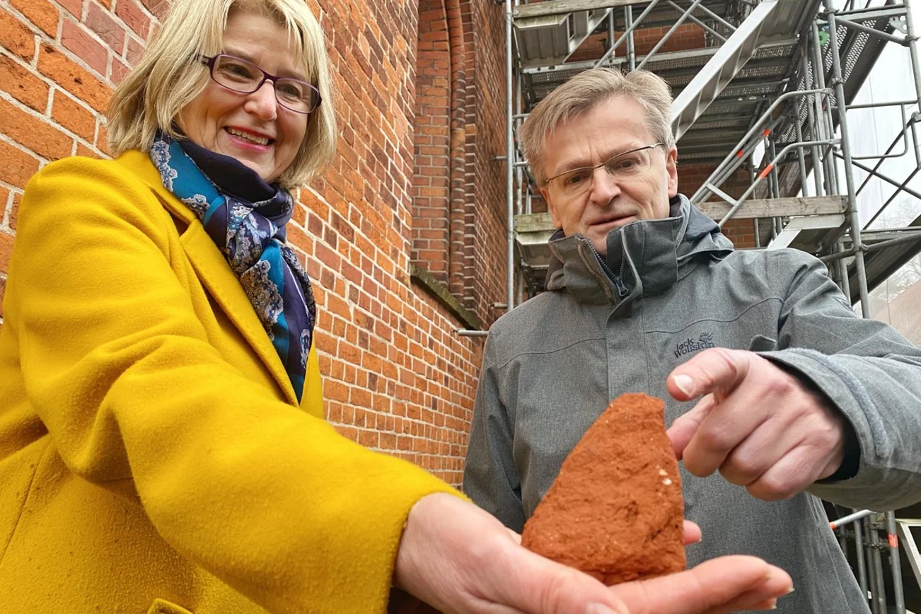 Zwei Personen stehen am Baugerüst des Ratzeburger Doms und schauen auf einen Stein. 