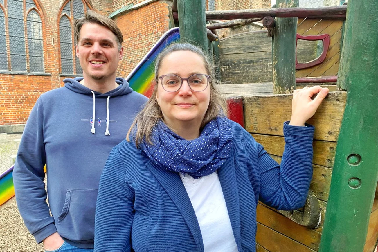 Ein Mann und eine Frau stehen an einem Spielgerät und Kinder und schauen in die Kamera. 