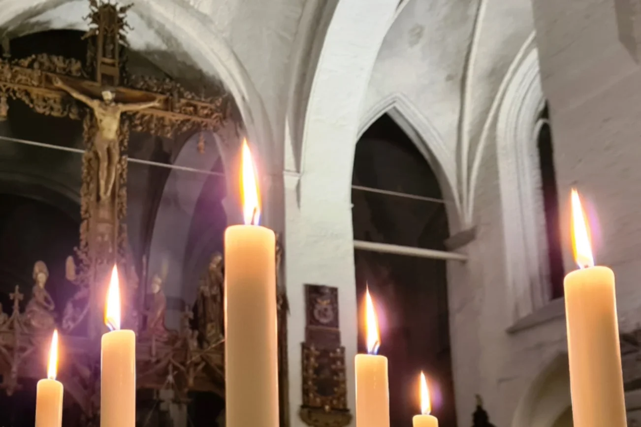 Im Vordergrund brennen Kerzen. Sie leiten den Blick auf den gekreuzigten Jesus am Triumphkreuz im Dom zu Lübeck.