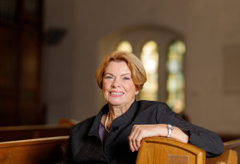 Eine Frau sitzt lächelnd in einer Kirche.  - Copyright: Marcelo Hernandez, Nordkirche