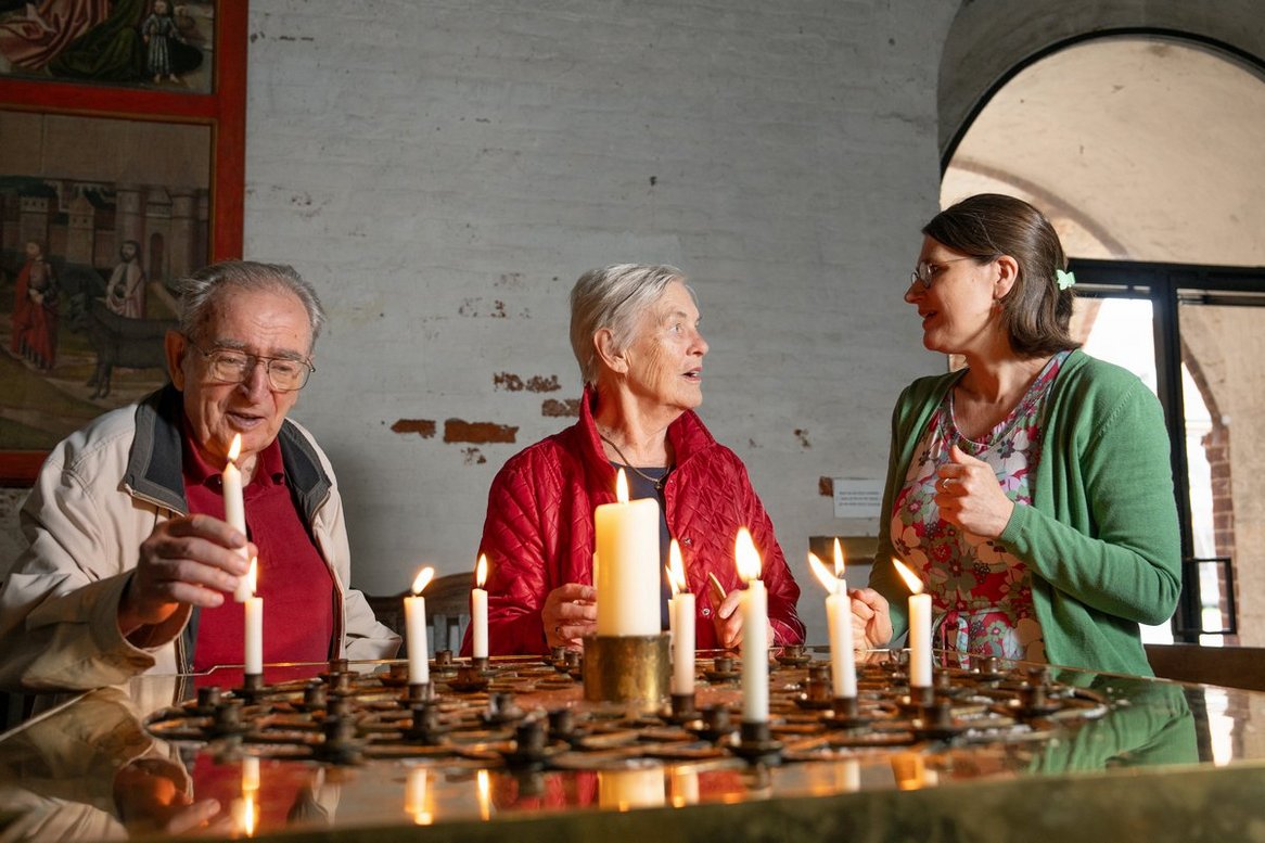 Copyright: Oliver Beck Ein älteres Paar steht mit einer jüngeren Frau an einem Kerzentisch.