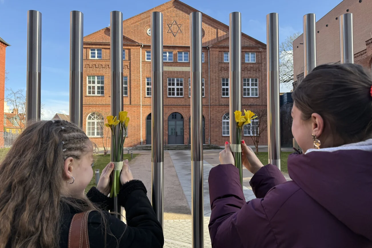 Zwei junge Frauen befestigen Blumen am Zaun einer Synagoge.
