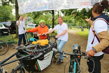 Zwei Männer fahren mit dem Fahrrad unter einen Banner hindurch. - Copyright: Thomas Biller