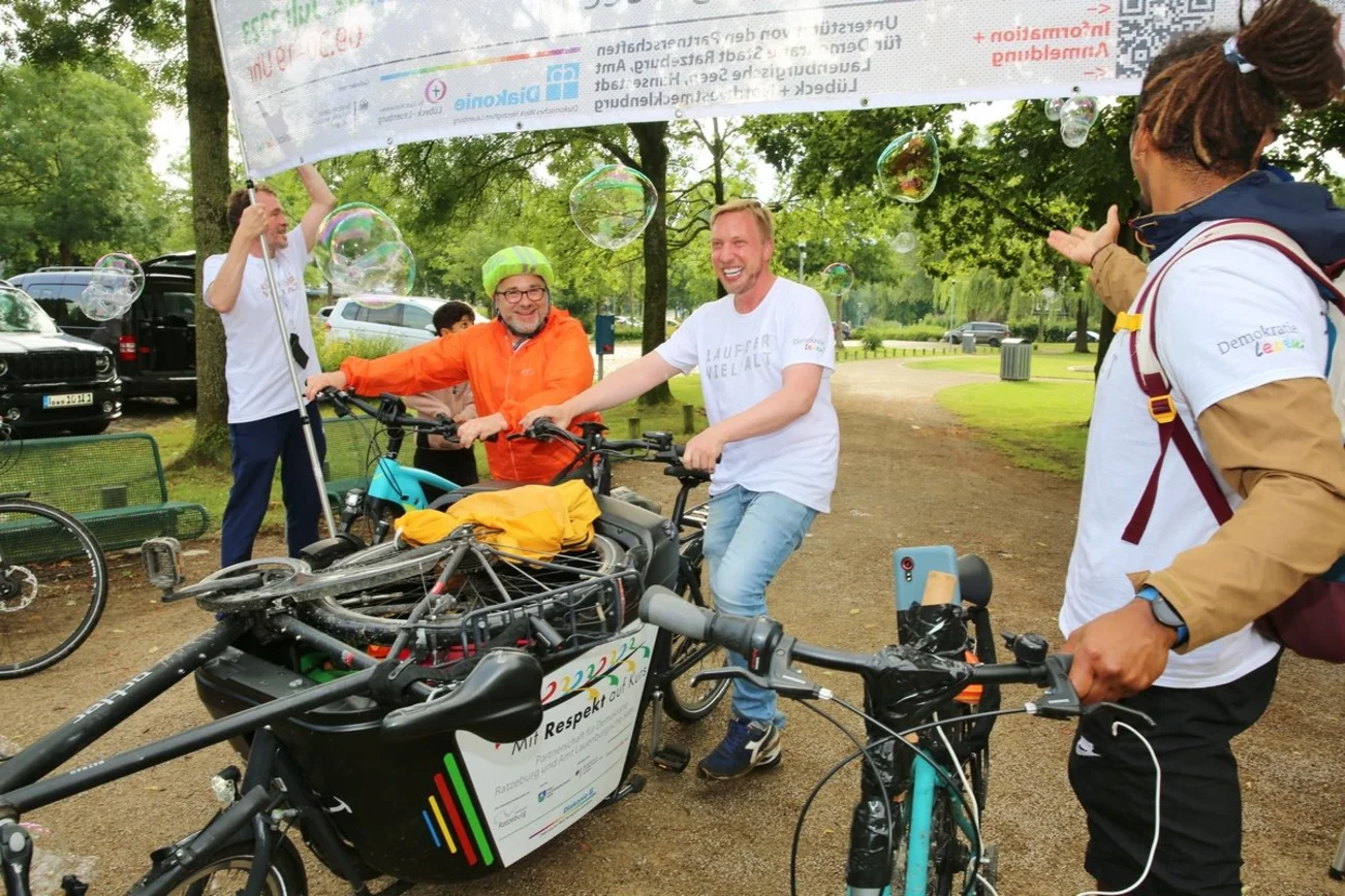 Zwei Männer fahren mit dem Fahrrad unter einen Banner hindurch.