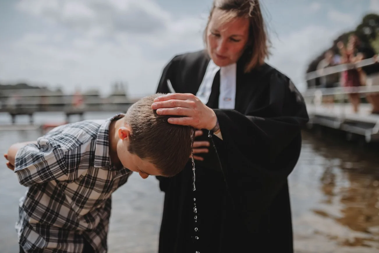Eine Pastorin tauft einen Jungen im Wasser.