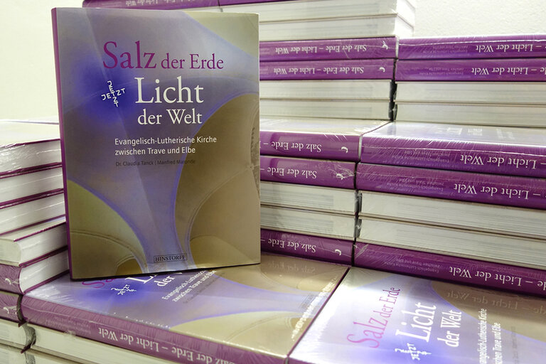 Buchband „Salz der Erde – Licht der Welt": Mehrere übereinandergestapelte Bücher dieses Buchbandes. Ein Buch steht aufrecht mit dem Buchdeckel nach vorne