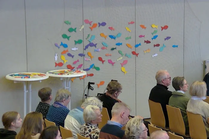 Bunte Papierfische an einer Wand, davor sitzen mehrere Personen