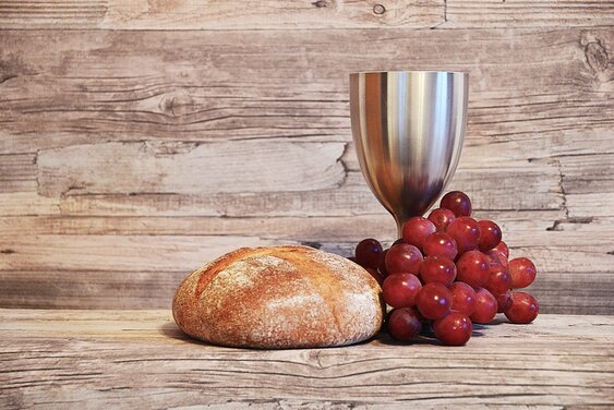 Silberner Kelch, Brot und Weintrauben vor eine Holzwand - Copyright: N. Schwarz © GemeindebriefDruckerei.de