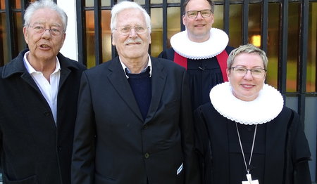 Vier Personen stehen vor einer Kirche. 