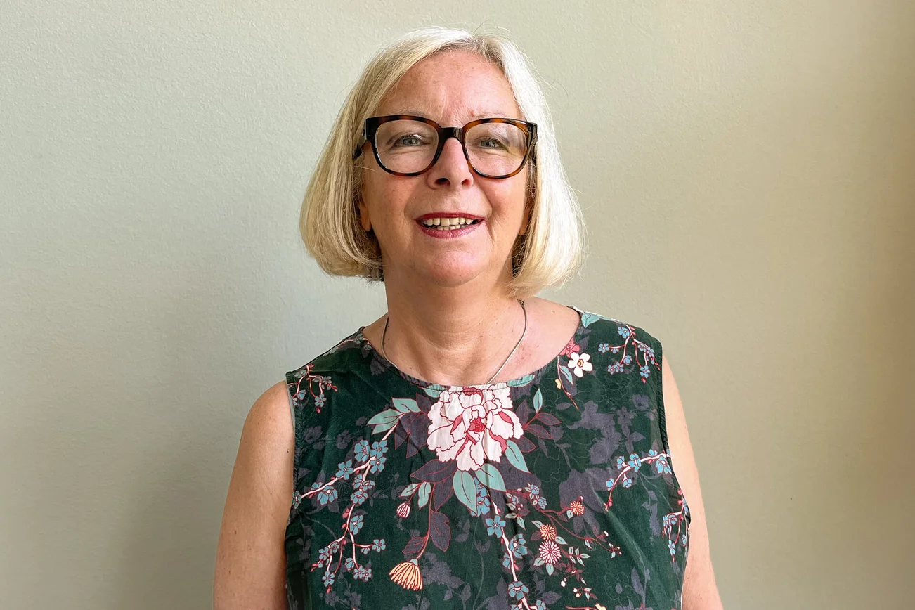 Eine Frau mit grauen kinnlangen Haaren und Brille lächelt in die Kamera.