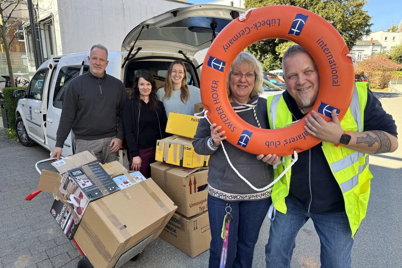 Menschen mit Mützen und einem Rettungsring stehen vor einem Auto.