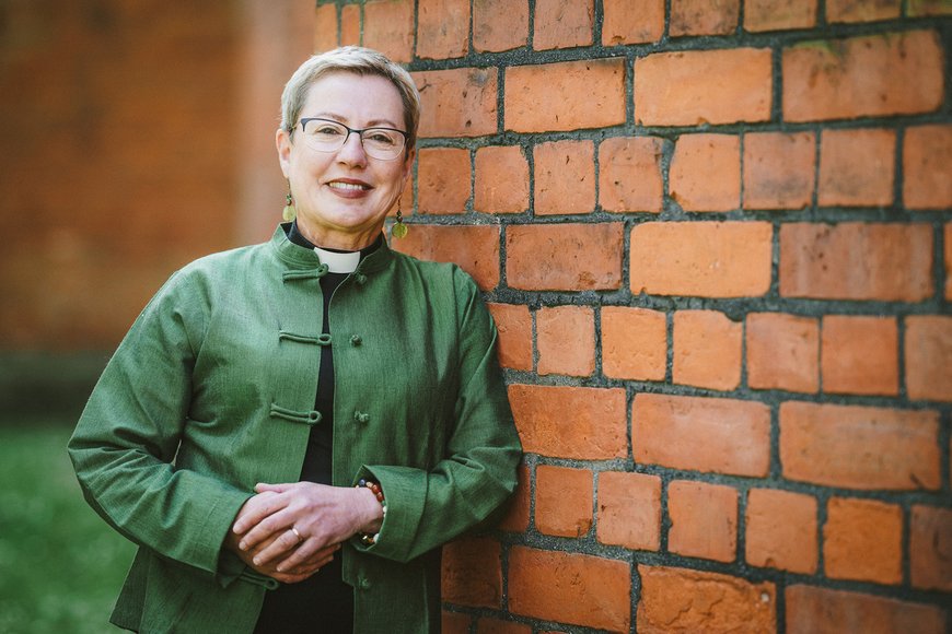 Frau lehtn sich an eine Backsteinmauer und lächelt die Betrachtenden an. - Copyright: Guido Kollmeier