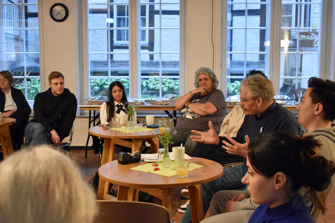 Verschiende Menschen sitzen an Tischen und sind im Gespräch.