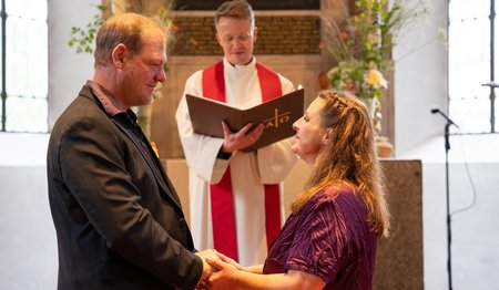 Ein Paar steht vor einem Pastor am Altar und schaut einander in die Augen. 