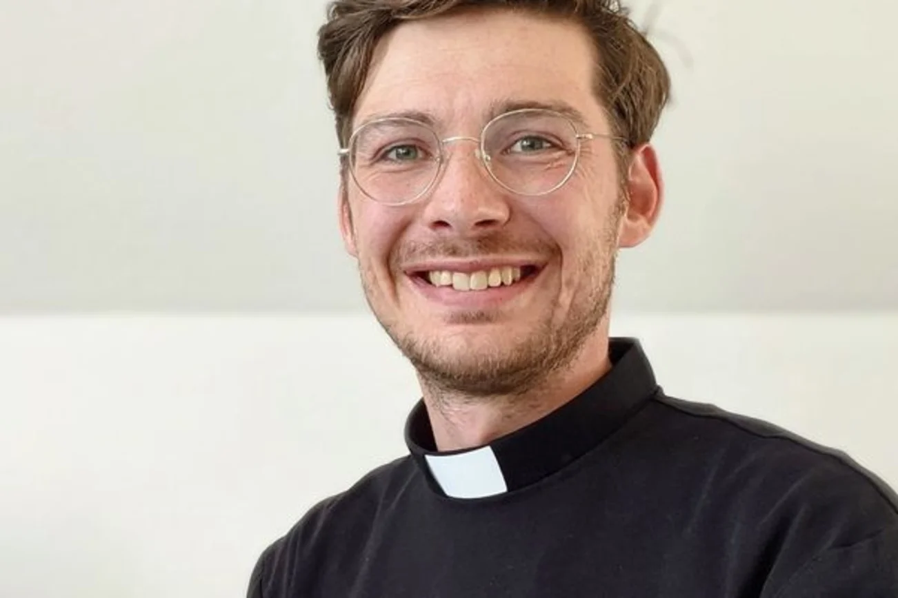 Junger Mann im Talar lächelt in die Kamera.