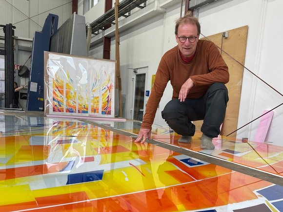 Ein Mann hockt auf den Glasfronten in der Glaswerkstatt.