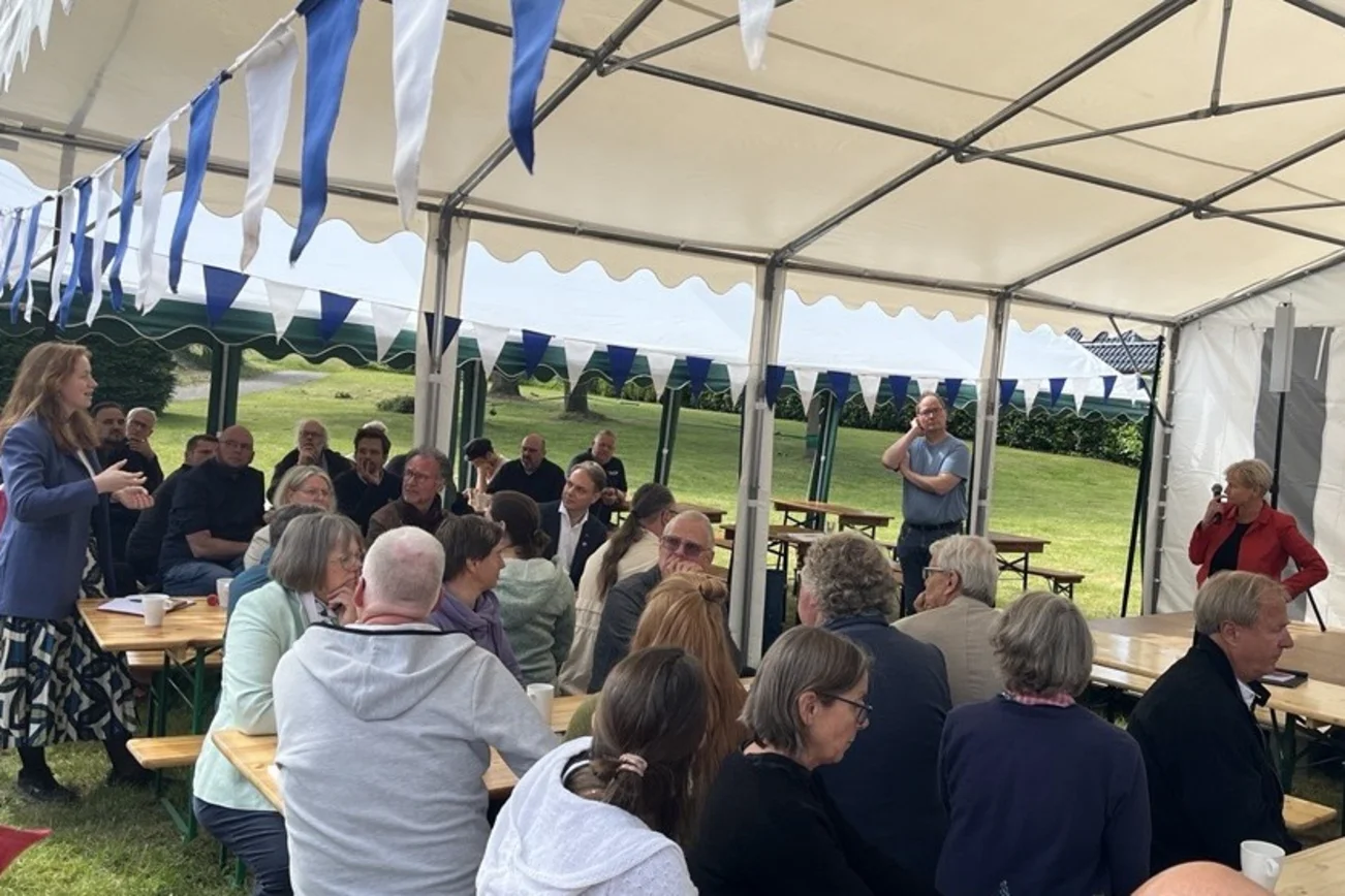 Menschen in einem Festzelt auf Bierbänken.