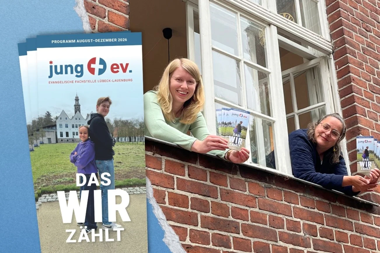 Zwei Frauen schauen aus einem Fenster und halten Flyer in den Händen.