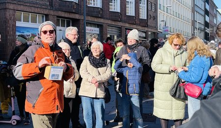 Eine Gruppe Menschen mit Jacken und Mützen bekleidet stehen in der Sonne