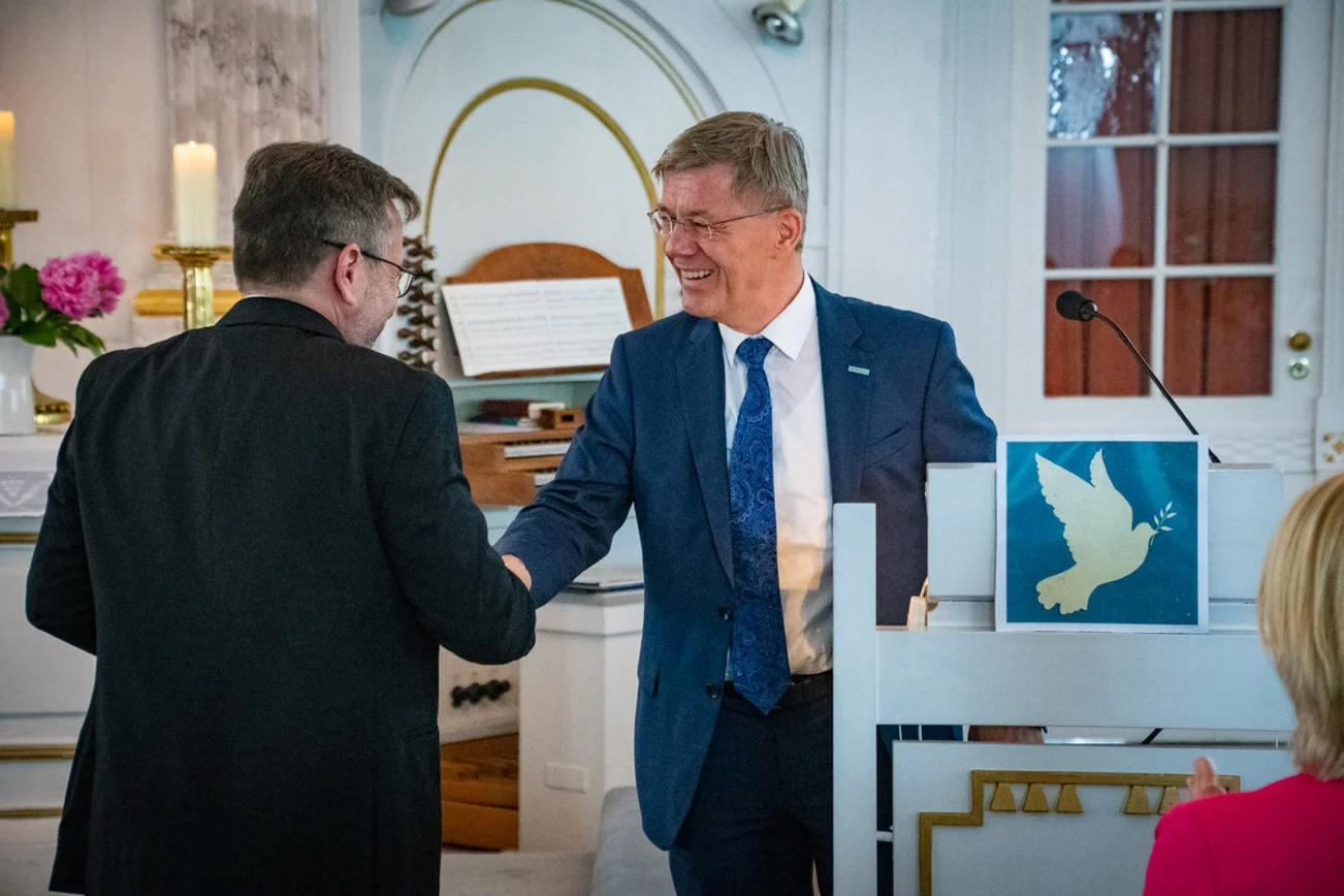 Zwei Männer reichen sich die Hände in einer Kirche. 