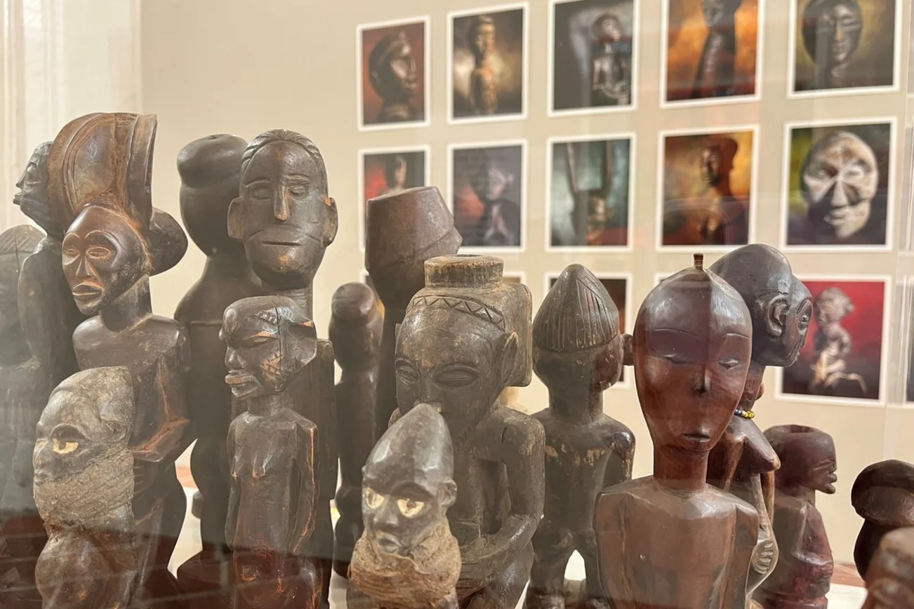 Eine Reihe afrikanischer Holzschnitzereien vor einer Wand mit Fotografien
