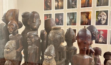 Eine Reihe afrikanischer Holzschnitzereien vor einer Wand mit Fotografien